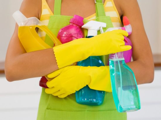 Cleaning person yellow gloves holding cleaning supplies.