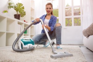 A woman is sitting on the floor with a vacuum cleaner.