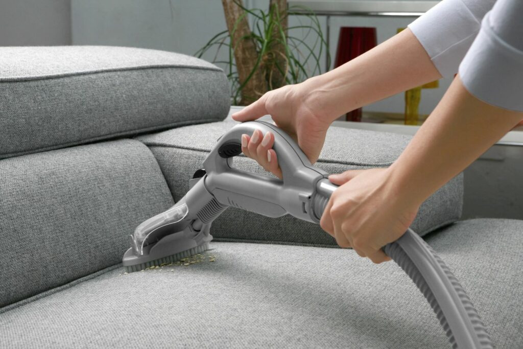 A person is using the vacuum to clean the couch.