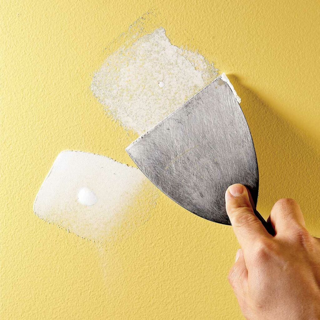 A person is holding a spatula and spreading glue on the wall.