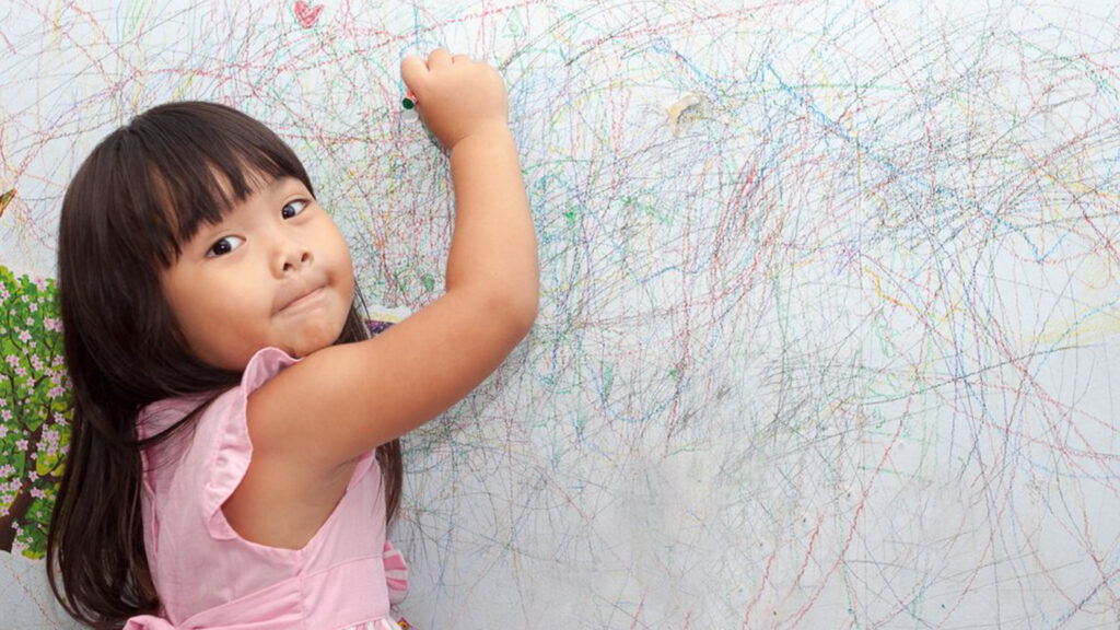 A little girl drawing on the wall with a marker.