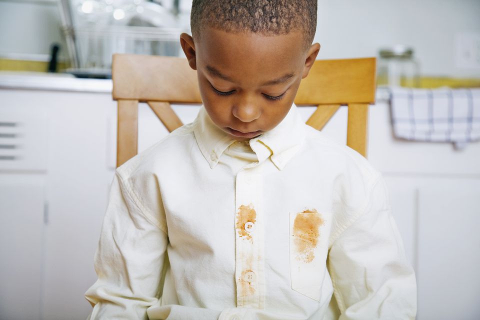 A young boy sitting in a chair with brown stains on his shirt.