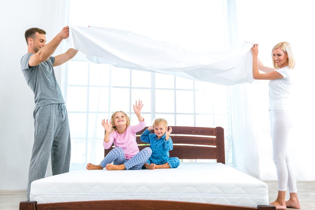 Two children sitting on a bed with sheets flying in the air.