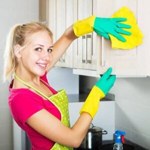 A woman in yellow gloves cleaning the kitchen.