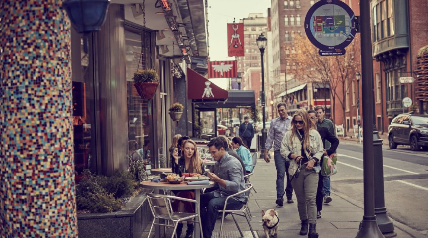 A group of people sitting at tables on the sidewalk.