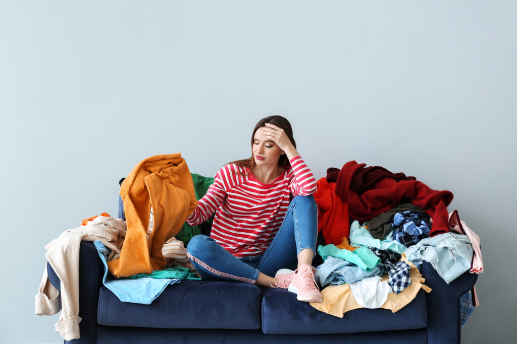 A woman sitting on top of a couch with lots of clothes.