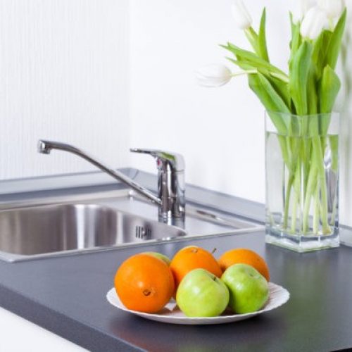 A bowl of fruit on the counter in front of a sink.