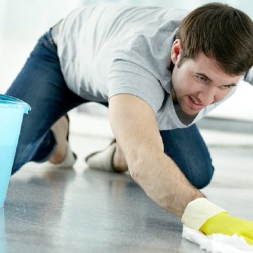 Young man washing floor in protective gloves A man cleaning the floor with a yellow glove.