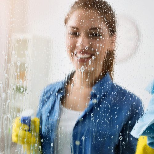 Cleaning window with special cleaner A woman in blue shirt holding a spray bottle.